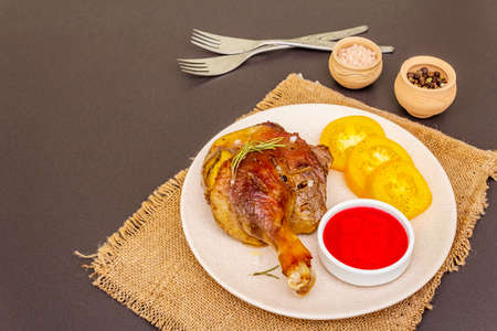 Crusty roasted duck leg. Traditional French food confit preparation. Served with cranberry sauce, fresh tomatoes, dry rosemary. Animal proteins, healthy fats. Stone background copy spaceの写真素材