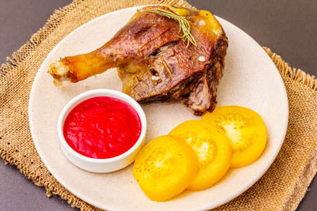 Crusty roasted duck leg. Traditional French food confit preparation. Served with cranberry sauce, fresh tomatoes, dry rosemary. Animal proteins, healthy fats. Stone background close upの写真素材
