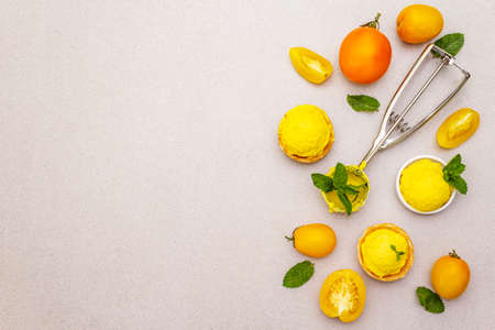 Yellow tomato ice cream, sorbet, gelato. Summer healthy refreshment dessert. Vegetarian (vegan) trendy food concept. With fresh vegetables and mint. Stone concrete background, copy space, top viewの写真素材