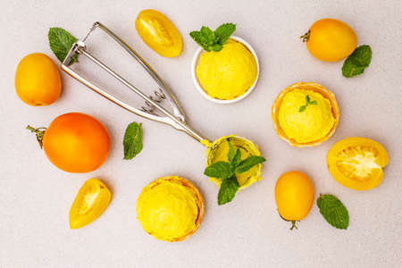 Yellow tomato ice cream, sorbet, gelato. Summer healthy refreshment dessert. Vegetarian (vegan) trendy food concept. With fresh vegetables and mint. Stone concrete background, top viewの写真素材