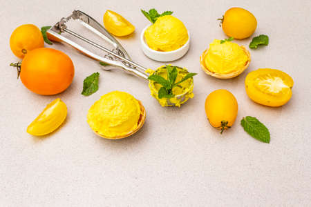 Yellow tomato ice cream, sorbet, gelato. Summer healthy refreshment dessert. Vegetarian (vegan) trendy food concept. With fresh vegetables and mint. Stone concrete background, copy spaceの写真素材
