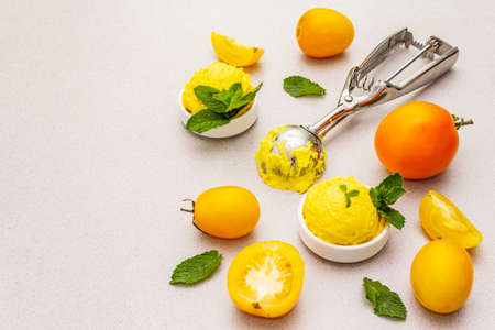 Yellow tomato ice cream, sorbet, gelato. Summer healthy refreshment dessert. Vegetarian (vegan) trendy food concept. With fresh vegetables and mint. Stone concrete background, copy spaceの写真素材