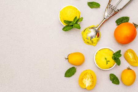 Yellow tomato ice cream, sorbet, gelato. Summer healthy refreshment dessert. Vegetarian (vegan) trendy food concept. With fresh vegetables and mint. Stone concrete background, copy space, top viewの写真素材