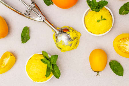 Yellow tomato ice cream, sorbet, gelato. Summer healthy refreshment dessert. Vegetarian (vegan) trendy food concept. With fresh vegetables and mint. Stone concrete background, top viewの写真素材