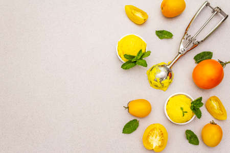 Yellow tomato ice cream, sorbet, gelato. Summer healthy refreshment dessert. Vegetarian (vegan) trendy food concept. With fresh vegetables and mint. Stone concrete background, copy space, top viewの写真素材