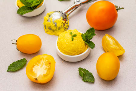 Yellow tomato ice cream, sorbet, gelato. Summer healthy refreshment dessert. Vegetarian (vegan) trendy food concept. With fresh vegetables and mint. Stone concrete background, close upの写真素材