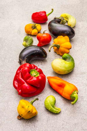 Trendy ugly organic vegetables. Assortment of fresh pepper, eggplant, cucumber, tomato, pumpkin. Cooking ugly food concept. Stone concrete background, close upの写真素材