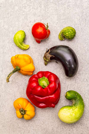 Trendy ugly organic vegetables. Assortment of fresh pepper, eggplant, cucumber, tomato, pumpkin. Cooking ugly food concept. Stone concrete background, top view, close upの写真素材
