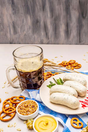 Oktoberfest set. Dark beer, weisswurst, pretzels, mustard, spikelets of grain, hop. Traditional German cuisine, festival food. Mug, linen napkin, stone concrete background, wooden backdrop copy spaceの写真素材
