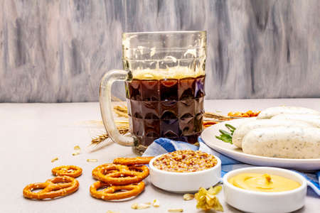 Oktoberfest set. Dark beer, weisswurst, pretzels, mustard, spikelets of grain, hop. Traditional German cuisine, festival food. Mug, linen napkin, stone concrete background, wooden backdrop copy spaceの写真素材