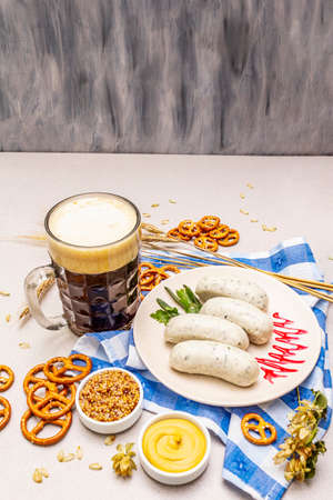 Oktoberfest set. Dark beer, weisswurst, pretzels, mustard, spikelets of grain, hop. Traditional German cuisine, festival food. Mug, linen napkin, stone concrete background, wooden backdrop copy spaceの写真素材