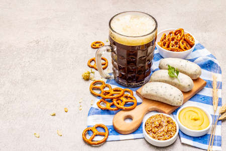 Oktoberfest set. Dark beer, weisswurst, pretzels, mustard, spikelets of grain, hop. Traditional German cuisine, festival food. Mug, linen napkin, stone concrete background copy spaceの写真素材