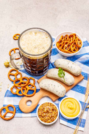 Oktoberfest set. Dark beer, weisswurst, pretzels, mustard, spikelets of grain, hop. Traditional German cuisine, festival food. Mug, linen napkin, stone concrete background close upの写真素材