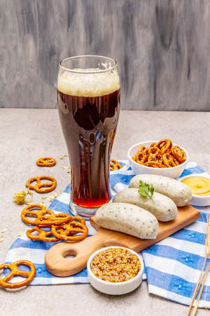 Oktoberfest set. Dark beer, weisswurst, pretzels, mustard, spikelets of grain, hop. Traditional German cuisine, festival food. Mug, linen napkin, stone concrete background copy spaceの写真素材