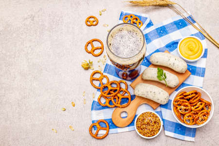 Oktoberfest set. Dark beer, weisswurst, pretzels, mustard, spikelets of grain, hop. Traditional German cuisine, festival food. Mug, linen napkin, stone concrete background copy space top viewの写真素材