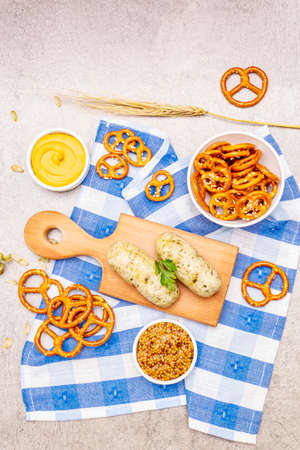 Oktoberfest set. White sausage weisswurst, pretzels, mustard, spikelets of grain, hop. Traditional German cuisine, festival food. Bowls, linen napkin, stone concrete background top viewの写真素材