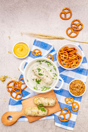 Oktoberfest set. White sausage weisswurst, pretzels, mustard, spikelets of grain, hop. Traditional German cuisine, festival food. Bowls, linen napkin, stone concrete background top viewの写真素材