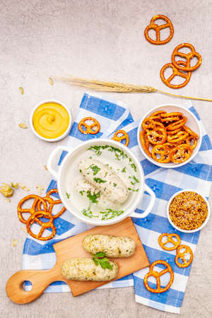 Oktoberfest set. White sausage weisswurst, pretzels, mustard, spikelets of grain, hop. Traditional German cuisine, festival food. Bowls, linen napkin, stone concrete background top viewの写真素材