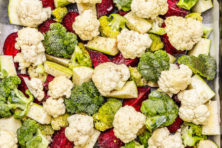 Assorted fresh vegetables on a baking tray. Cauliflower, broccoli, beet, zucchini. Sea salt, ground black pepper, olive oil. Healthy food concept, close up, top viewの写真素材