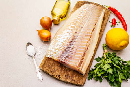 Raw cod loin fillet with vegetables, spice, olive oil and salt. Freshly thawed fish, healthy vegetarian food concept. Old wooden cutting board, stone concrete background copy space top viewの写真素材