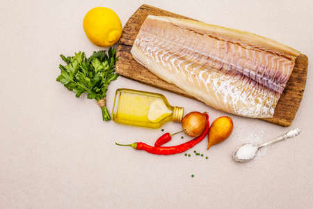 Raw cod loin fillet with vegetables, spice, olive oil and salt. Freshly thawed fish, healthy vegetarian food concept. Old wooden cutting board, stone concrete background copy spaceの写真素材