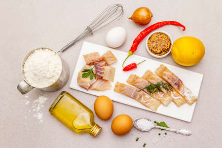 Raw cod loin fillet with vegetables, spice, eggs, olive oil and flour. Freshly thawed fish, ingredients and equipment for for frying on batter or baking. Stone background top viewの写真素材