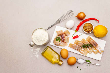 Raw cod loin fillet with vegetables, spice, eggs, olive oil and flour. Freshly thawed fish, ingredients and equipment for for frying on batter or baking. Stone background copy space top viewの写真素材