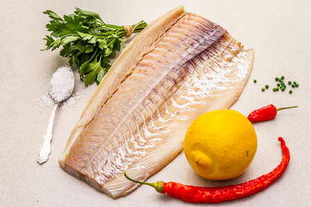 Raw cod loin fillet with lemon, sea salt, chili and cayenne pepper, parsley. Freshly thawed fish, healthy vegetarian food concept. Stone concrete background close upの写真素材