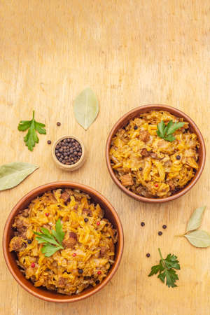 Stewed (braised) cabbage served on ethnic ceramic bowl. Traditional Polish Bigos with meat, aromatic pepper, fresh parsley. Rustic wooden background, copy space, top viewの写真素材