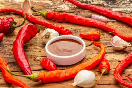 Traditional Thai sauce Sriracha with ingredients. Slightly dried red and orange chilli, garlic. In ceramic bowl, wooden bark background, close upの写真素材