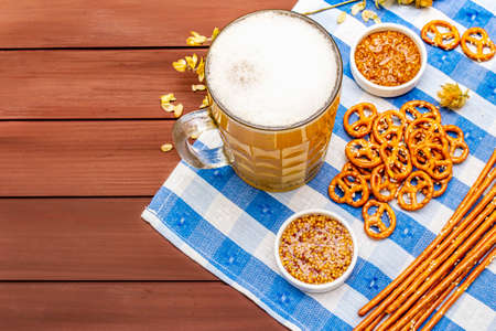 Oktoberfest set. Light beer, pretzels, mustard, sesame straw, hop. Traditional German cuisine, festival food. Bottles, linen napkin, wooden boards background, copy space, top viewの写真素材