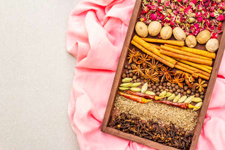 Ras el Hanout, exotic luxury spice. Ingredients for preparation oriental spice mix in wooden box. An essential spice for any Moroccan dishes. Stone background, pink cloth copy space top view close upの写真素材