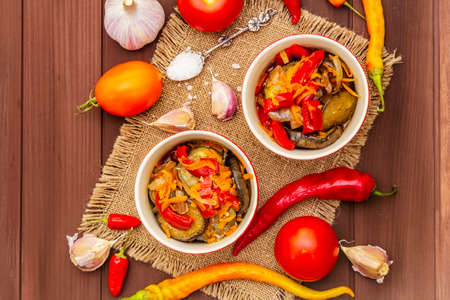 Marinated salad with pickled vegetables: eggplant, carrot, pepper, tomato, garlic. Healthy food concept, autumn harvest products recipe. Wooden boards background, top viewの写真素材
