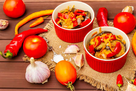 Marinated salad with pickled vegetables: eggplant, carrot, pepper, tomato, garlic. Healthy food concept, autumn harvest products recipe. Wooden boards background, close upの写真素材