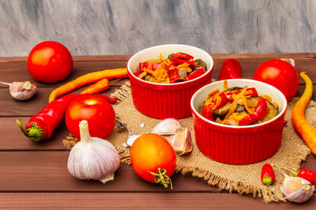 Marinated salad with pickled vegetables: eggplant, carrot, pepper, tomato, garlic. Healthy food concept, autumn harvest products recipe. Wooden boards background, copy spaceの写真素材