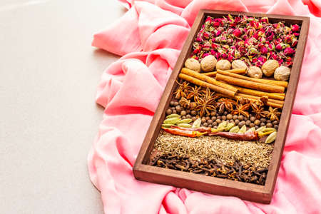 Ras el Hanout, exotic luxury spice with rose petals. Ingredients for preparation oriental spice mix in wooden box. An essential spice for any Moroccan dishes. Stone background, pink cloth copy spaceの写真素材