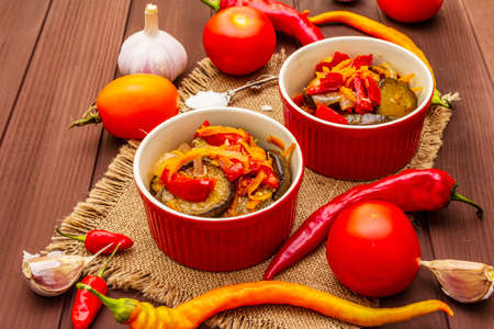 Marinated salad with pickled vegetables: eggplant, carrot, pepper, tomato, garlic. Healthy food concept, autumn harvest products recipe. Wooden boards background, copy space, close upの写真素材