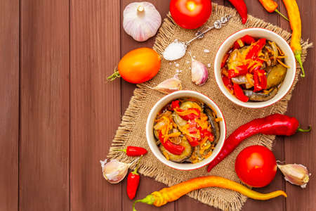 Marinated salad with pickled vegetables: eggplant, carrot, pepper, tomato, garlic. Healthy food concept, autumn harvest products recipe. Wooden boards background, copy space, top viewの写真素材