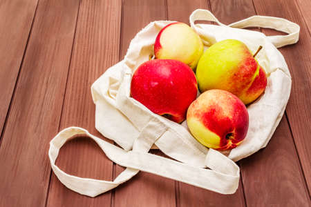 Eco friendly packaging, zero waste for free plastic shopping. Recycled materials lifestyle concept. Fresh apples and peaches in textile bag. Wooden boards background, copy space, close upの写真素材