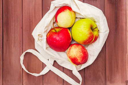 Eco friendly packaging, zero waste for free plastic shopping. Recycled materials lifestyle concept. Fresh apples and peaches in textile bag. Wooden boards background, top view, close upの写真素材