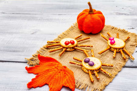 Funny kids food. Edible spiders from cookies, small candies and sweet sesame sticks. Halloween concept with autumn leaves, pumpkin. Vintage sackcloth, wooden boards background, copy space, close upの写真素材