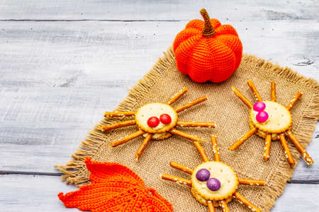Funny kids food. Edible spiders from cookies, small candies and sweet sesame sticks. Halloween concept with autumn leaves, pumpkin. Vintage sackcloth, wooden boards background, copy spaceの写真素材