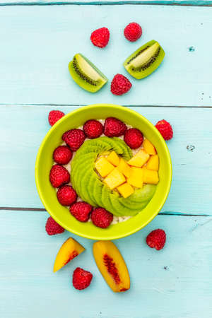 Oatmeal bowl with fresh berries and fruits. Healthy breakfast nutrition concept, vegetarian (vegan) food. Homemade vitamin eating, good mood. Turquoise wooden background, copy space top view close upの写真素材