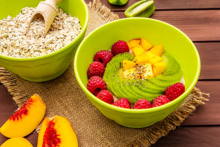 Oatmeal bowl with fresh berries and fruits. Healthy breakfast nutrition concept, vegetarian (vegan) food. Homemade vitamin eating, good mood. Wooden boards background, close upの写真素材