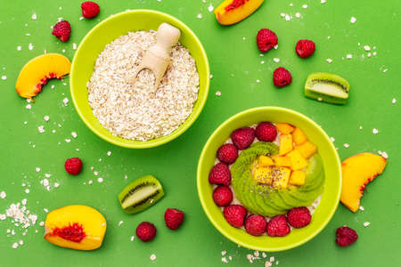Oatmeal bowl with fresh berries and fruits. Healthy breakfast nutrition concept, vegetarian (vegan) food. Homemade vitamin eating, good mood. Bright green background, top view, close upの写真素材