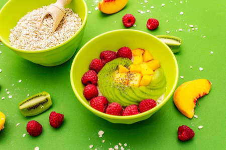 Oatmeal bowl with fresh berries and fruits. Healthy breakfast nutrition concept, vegetarian (vegan) food. Homemade vitamin eating, good mood. Bright green background, close upの写真素材