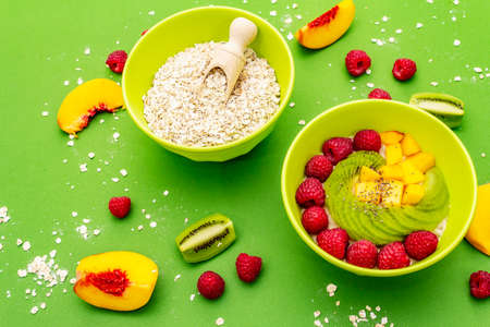 Oatmeal bowl with fresh berries and fruits. Healthy breakfast nutrition concept, vegetarian (vegan) food. Homemade vitamin eating, good mood. Bright green background, close upの写真素材