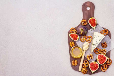 Cheese platter (board) with blue cheese, honey, walnuts, figs, pretzels. Traditional healthy appetizer, snack. Wooden rustic board on stone concrete background, copy space, top viewの写真素材