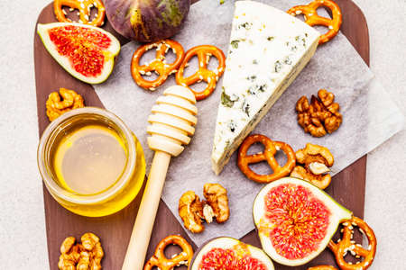 Cheese platter (board) with blue cheese, honey, walnuts, figs, pretzels. Traditional healthy appetizer, snack. Wooden rustic board on stone concrete background, top view, close upの写真素材