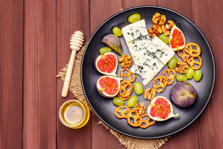 Cheese plate with blue cheese, honey, walnuts, figs, grapes, pretzels. Traditional healthy appetizer, snack, antipasti. Wooden boards background, vintage sackcloth, copy space, top view, close upの写真素材